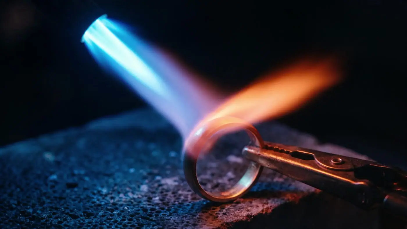 Lötflamme mit blauem Kegel spielt auf einem goldenen Ring auf einem Kohleblock